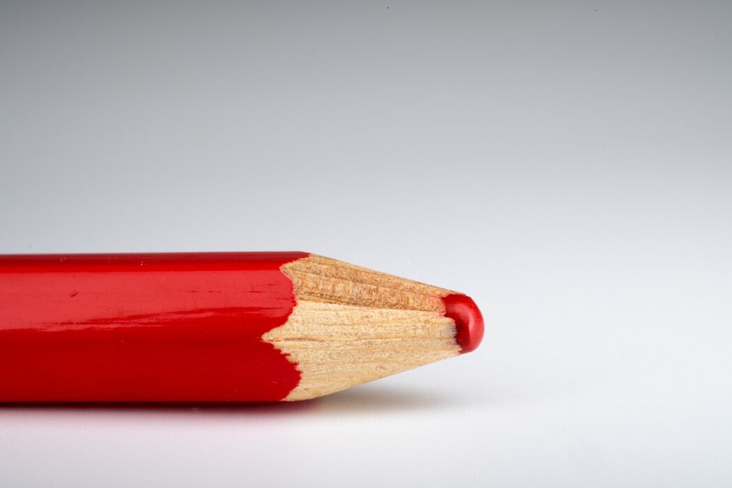 A red pencil crayon tip laid horizontally against a grey to white gradient background.