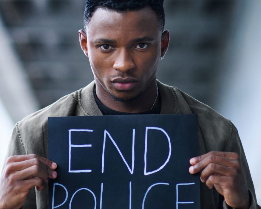 A Black man holds up a sign that reads end police.